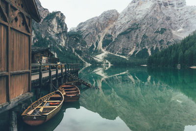 Boats moored in lake by houses against rocky mountains