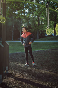 Man with hands on hip standing by gymnastics ring at park