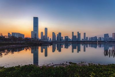 Reflection of buildings in city against sky during sunset