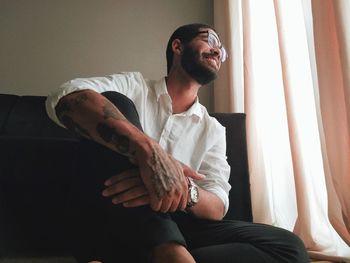 Young man looking away while sitting by window at home