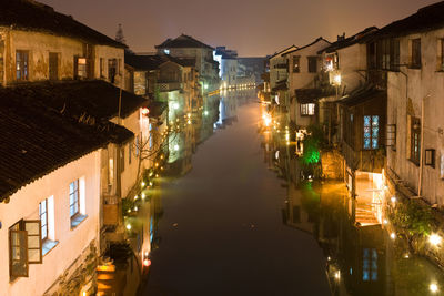 Illuminated street amidst buildings against sky at night