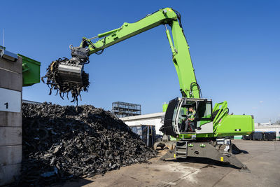 Mature man operating excavator and lifting rubber waste at recycling center