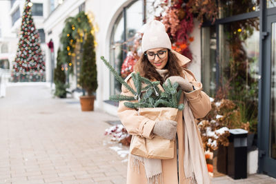 A stylish young woman straightens the branches of the nobilis walks through the christmas city