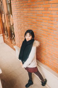 Portrait of smiling young woman standing against brick wall