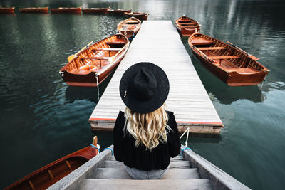 Rear view of woman sitting on pier over lake