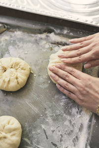 Cropped image of woman's hands kneading dough in tray at table