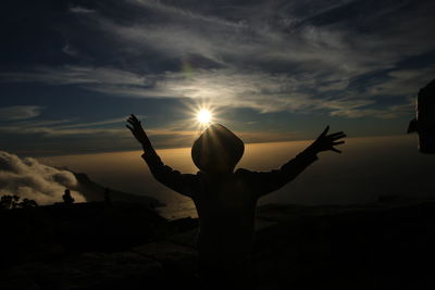 Silhouette woman with arms raised against sunset sky