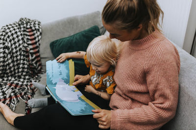 Mother reading toddler book on sofa