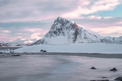 Scenic view of lake by snowcapped mountains against cloudy sky during sunset