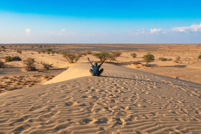 Rear view of a man sitting with arms outstretched on a sand dune at north horr sand dunes in kenya