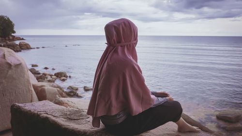 Woman sitting on beach looking at sea against sky