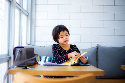 Cute girl reading book while sitting on sofa at home