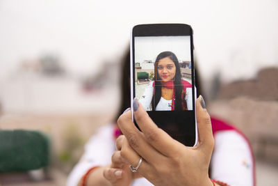 Portrait of young woman taking selfie against sky