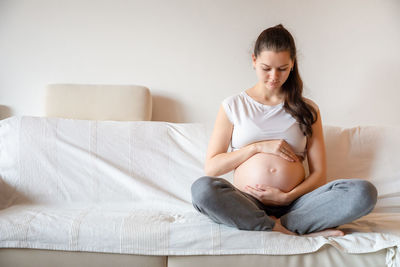 Young pregnant woman holding stomach sitting on sofa at home