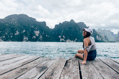 Side view of young woman sitting on pier over sea
