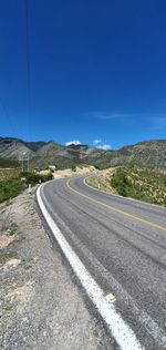 Road passing through landscape against clear blue sky