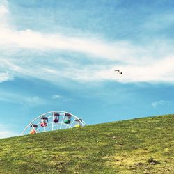 View of ferris wheel behind hill against sky