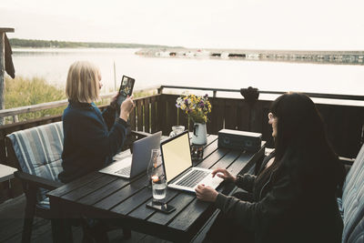 Woman using digital tablet while sitting with friends holding laptop at table in holiday villa