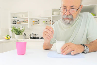 Senior man eating yogurt in the kitchen 