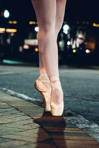 Low section of ballet dancer dancing on street at night