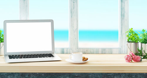 Close-up of laptop and breakfast on table by window