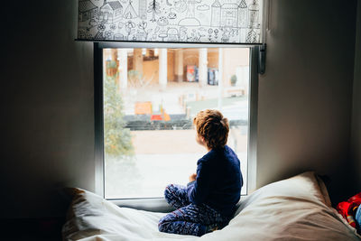 Rear view of boy looking through window at home