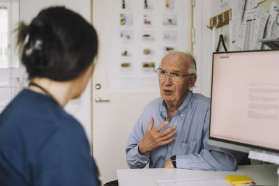 Senior male patient discussing with mature nurse during visit in clinic