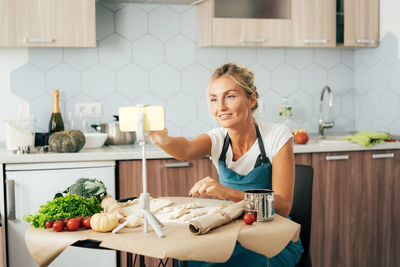 Pretty happy confident woman is cooking in the kitchen and watching a video recipe on the phone.