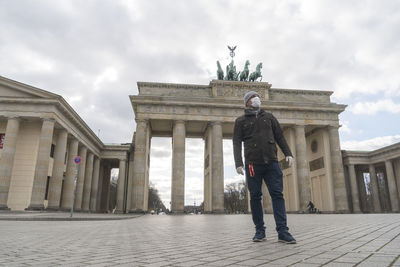 Tourist with medical mask and gloves posing alone in front of brandenburg gate during lockdown