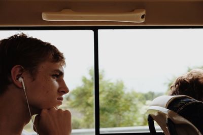 Side view of man listening music while traveling by window in bus