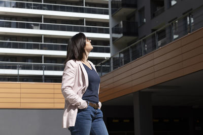 Happy mature 40 yo woman enjoys new apartment campus, complex in sunny day. female brunette wears