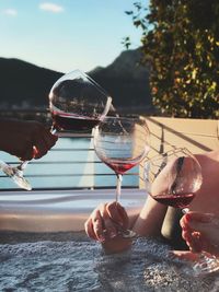 Close-up of hand holding wineglass against sky