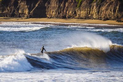 Man surfboarding in sea against mountain