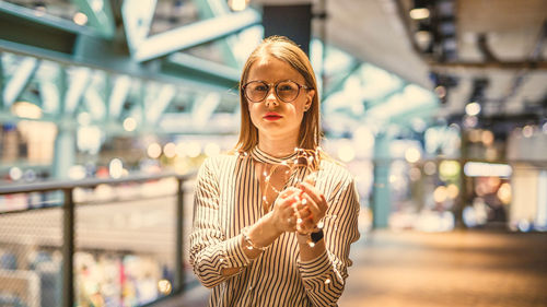 Portrait of young woman holding illuminated string lights