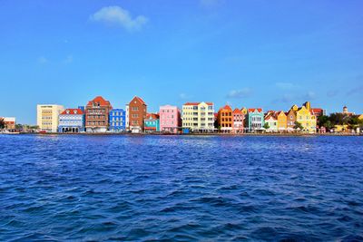 Sea by buildings against blue sky