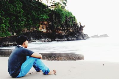 Side view of boy sitting on rock at beach