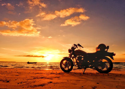 Bicycle on beach against sky during sunset