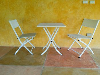 Table and chairs against yellow wall