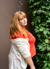 Young woman looking away while standing against plants