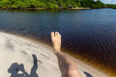 Photographer displays his shadow and leg in the photo against sand and water from a river