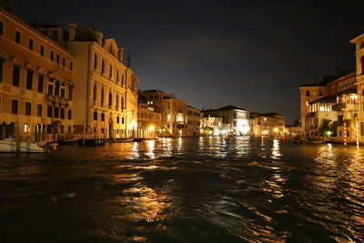 Buildings by river against sky at night