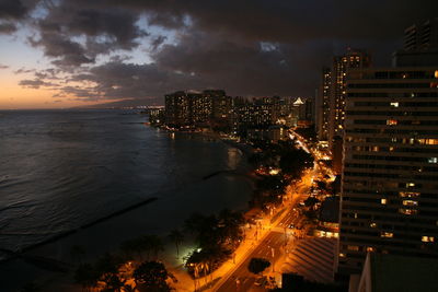 High angle view of illuminated buildings by sea against sky at night