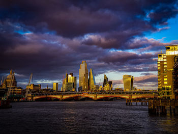 View of bridge over river and buildings against cloudy sky