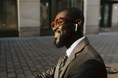 Smiling businessman with eyeglasses looking way while sitting on footpath