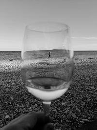 Close-up of hand holding wineglass against beach