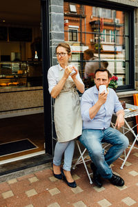 Man and woman, couple of cafe owners drinking tea at entrance of cafe