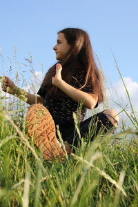 Young woman looking away on field against sky