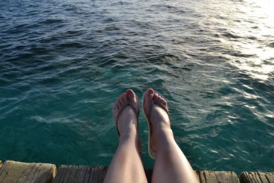 Low section of woman sitting on pier against sea