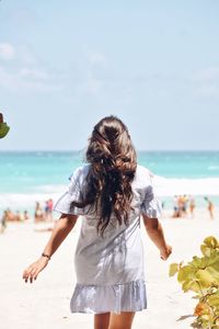 Rear view of woman standing at beach against sky