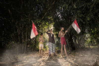 Man and boys with flags standing against trees in forest